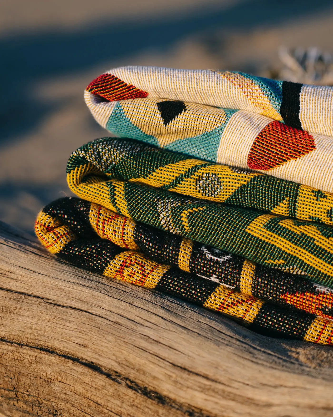 Stack of woven throw rugs on driftwood at the beach by Rug Lord