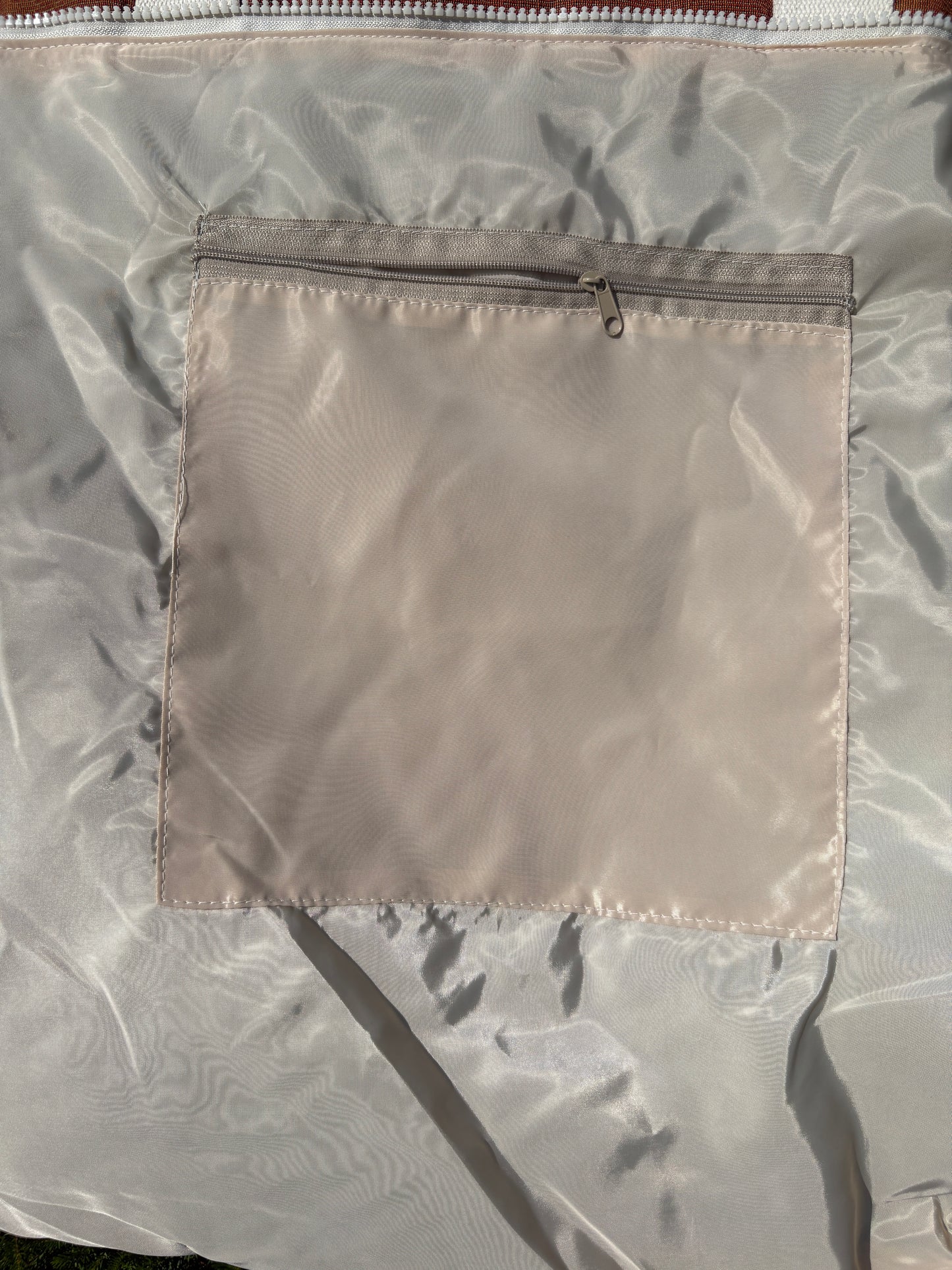 Close-up of a light beige nylon or polyester bag with a square zippered pocket on the front.