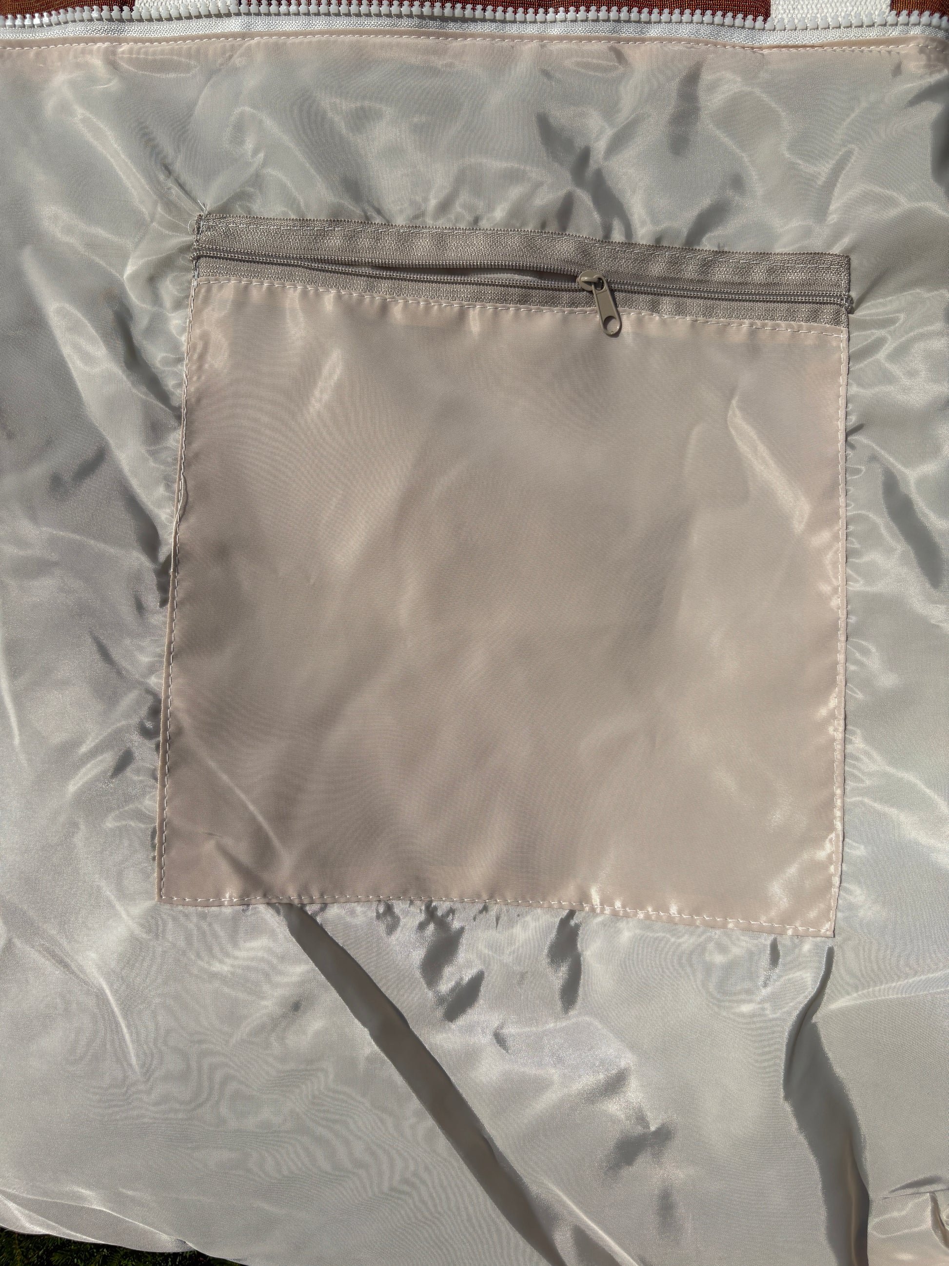 Close-up of a light beige nylon or polyester bag with a square zippered pocket on the front.