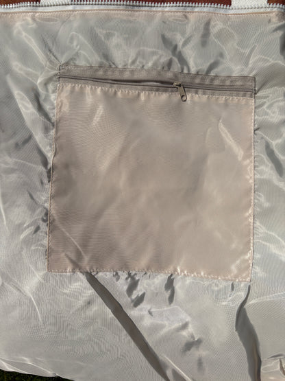 Close-up of a light beige nylon or polyester bag with a square zippered pocket on the front.